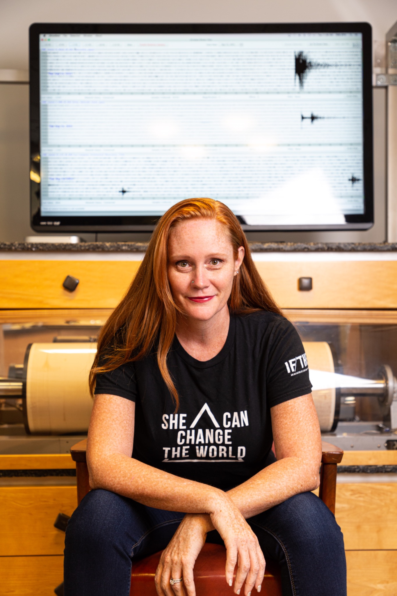 Wendy Bohon seated in a seismic laboratory wearing a She Can Change the World shirt.